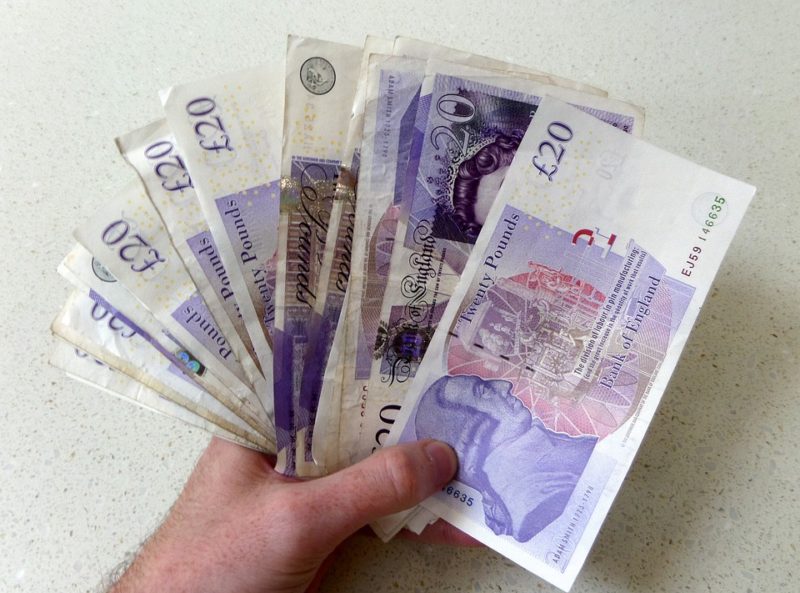 A photograph of a hand holding some £20 notes