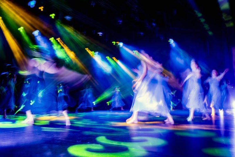 Blurred image shows dancers under coloured spotlights
